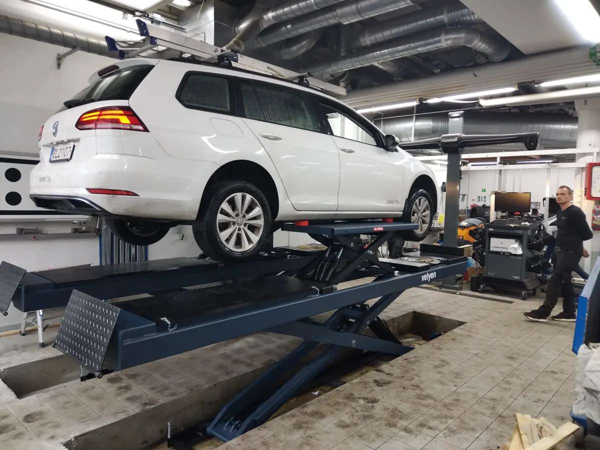 Asentaja tekemässä pyöränsuuntausta nostimella olevaan autoon